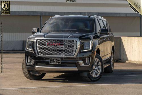 Front view of a black GMC Yukon Denali XL SUV parked in an urban setting, showcasing its prominent grille, headlights, and rugged design. The license plate area is visible.