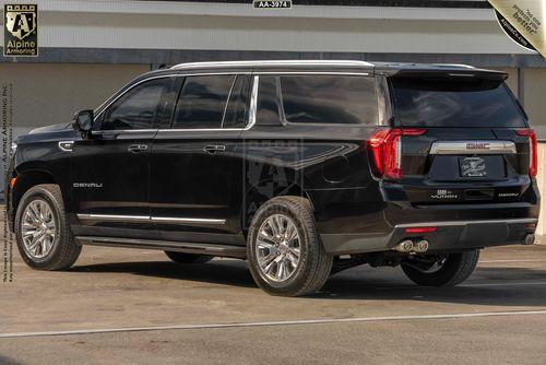 A black armored GMC Yukon Denali SUV is parked on a concrete surface. The vehicle is viewed from the rear.