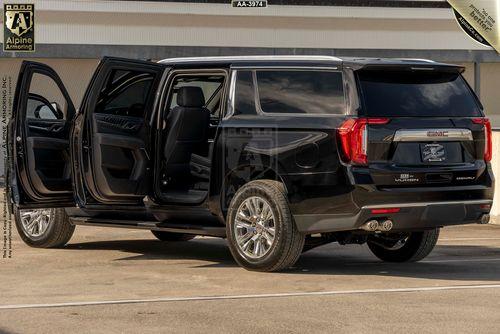 A black GMC Yukon Denali XL with its rear doors open, parked in an outdoor area with a building in the background.