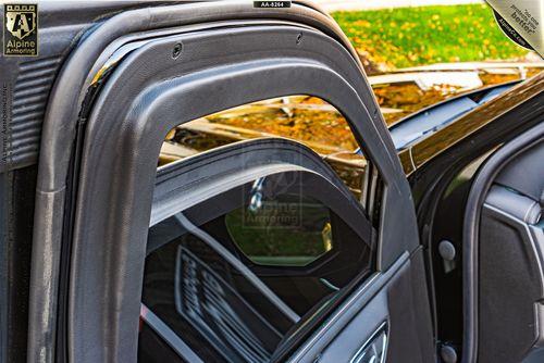 A close-up view of an armroed  GMC Yukon XL AT4 door showing the window partially rolled down and a label reading "Alpine Armoring." Background includes foliage.