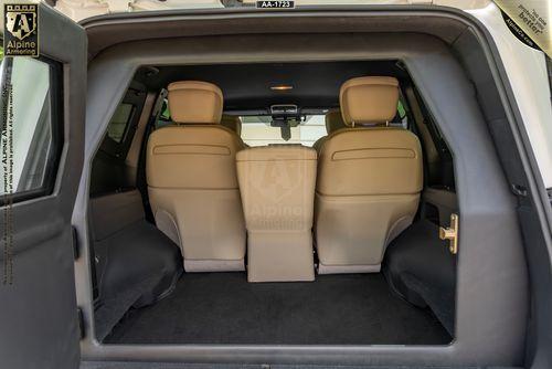 A view of an Armored Toyota Land Cruiser 300's interior from the open rear door, showing two beige leather front seats and a centrally aligned beige console.