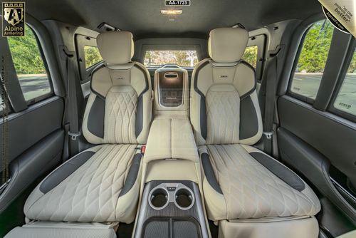 Spacious rear interior of an Armored Toyota Land Cruiser 300  with quilted beige leather seats, cup holders, and a window showing greenery outside.