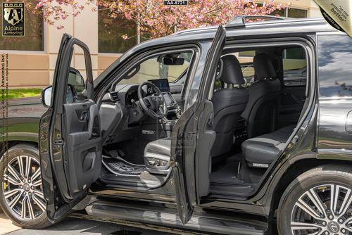 A black bulletproof Lexus LX600 Luxury SUV with both driver and passenger side doors open, revealing a plush interior with leather seats and a clean, modern dashboard.