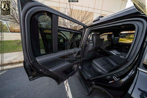 An open rear car door of a Lexus LX 600 Ultra Luxury reveals a black leather interior with spacious seating and a view of a building exterior through the windows.