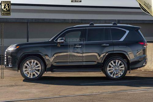 A black Lexus LX 600 Ultra Luxury is parked in front of a gray building. The vehicle has tinted windows and chrome wheels.