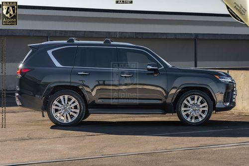 A dark gray armored Lexus LX600 Ultra Luxury SUV is parked in an outdoor area with a building in the background. The SUV has large alloy wheels and sleek design features.