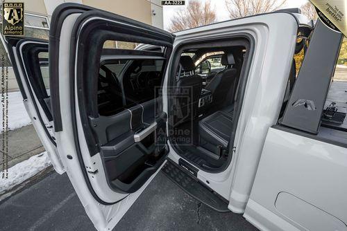 Open rear doors of a white Mastiff revealing two rows of black leather seats and interior features. The outside environment appears to be a parking area on a clear day.