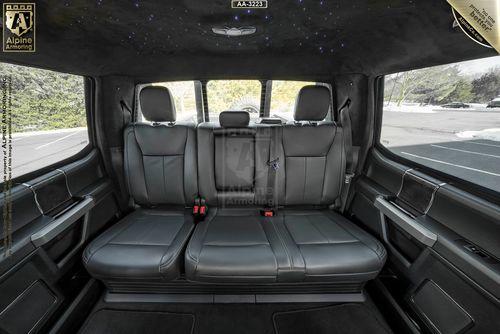 Interior of a Mastiff with black leather seating, armrests, and headrests, designed for spacious comfort. The roof features ambient star-like lighting. The scene outside shows a snowy landscape.