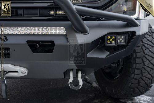 Close-up of a Mastiff's front bumper featuring a towing hook, spotlights, a row of LED lights, and a protective guard. The bumper has branding labels and is mounted on a large tire.