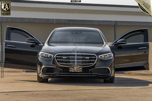 Front view of a black armored Mercedes-Benz S580 Executive sedan with both front doors open, parked outdoors in front of a modern building.