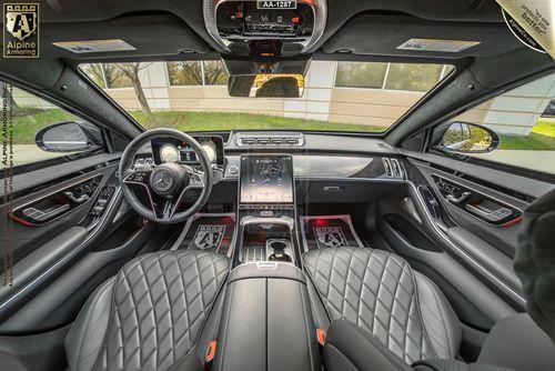 Interior view of a black armored Mercedes S580 Executive sedan featuring a leather-trimmed dashboard, quilted leather seats, a touchscreen display in the center console, and multiple control buttons on the steering wheel and dashboard.