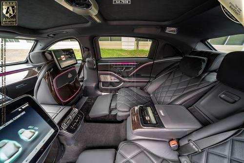 Interior of a luxurious Mercedes-Benz Maybach showcasing spacious black leather seats, high-tech control panels, and entertainment screens. The design features quilted stitching and modern amenities.