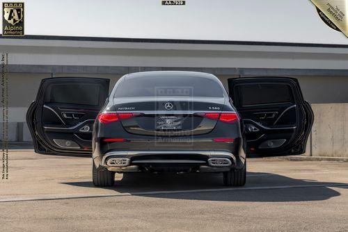 A black Mercedes Maybach sedan viewed from the rear with both back doors open in a parking area. The label "Alpine Armoring" is visible at the top of the image.