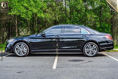 Side view of a black Mercedes-Benz 560 sedan parked in an outdoor lot with a background of green trees.