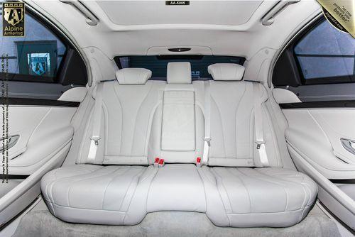 A spacious luxury Mercedes-Benz 560's rear seat featuring light grey leather upholstery, seat belts, and headrests. The interior is clean and includes a center armrest. The car's doors have metallic trim accents.