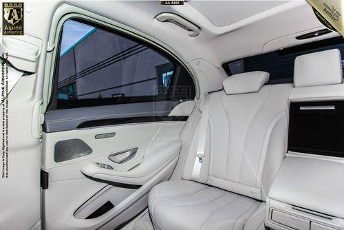 Interior of a Mercedes-Benz 560 showing white leather seats, a door with silver accents, and a small display screen. The backseat area appears spacious and well-illuminated.