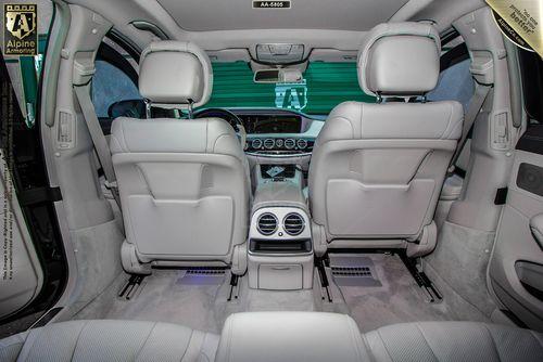 Interior view of a Mercedes 560  showing the back of the front seats, rear air vents, and a clean, sleek dashboard with multiple controls. The seats and cabin are upholstered in white leather.