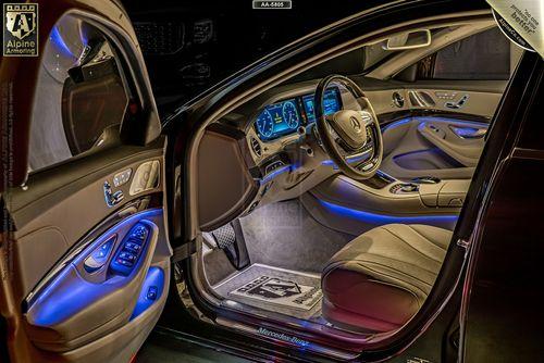 Interior view of a Mercedes-Benz 560  with illuminated dashboard, leather seats, and ambient lighting. The car features multiple digital displays, and the brand name is visible on the floor mat.