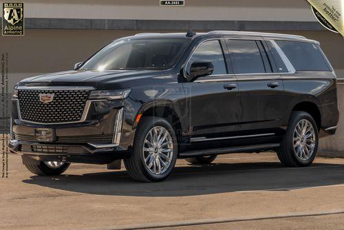 A black, armored Cadillac Escalade ESV Premium Luxury SUV with chrome accents is parked on a concrete surface. The vehicle is positioned at an angle, showing both the front and side. Branding and logo details are visible in the background.