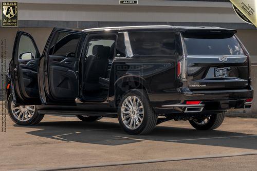 A black armored Cadillac Escalade ESV Premium Luxury with its rear passenger doors open, showcasing a spacious and upscale interior. The vehicle is parked in an outdoor area.