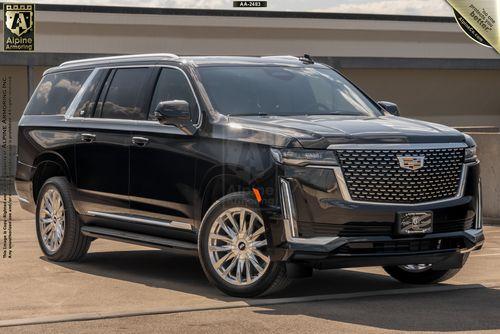 A black armored Cadillac Escalade ESV Premium Luxury SUV is parked outside on a clear day. The vehicle has a prominent grille, large wheels, and tinted windows.