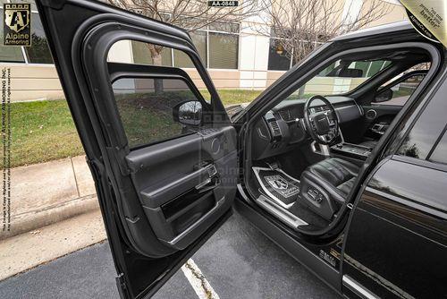 A black Range Rover Autobiography SUV with the driver's door open, revealing a black leather interior and a clean dashboard. The vehicle is parked on a street beside a beige and white building.