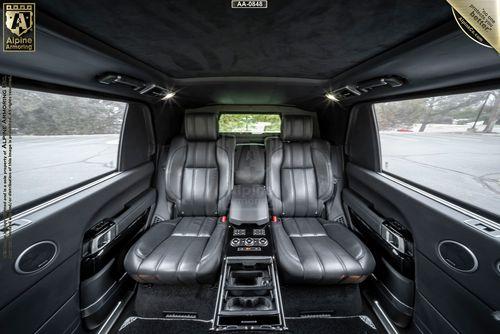 Luxurious car interior featuring black leather seats, a central console with controls, and side windows showcasing an outdoor view.