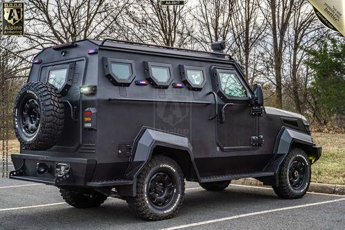 A black, armored SWAT APC CUDA is parked on a road with leafless trees in the background. The vehicle has rugged tires, a spare tire mounted on the rear, and small, reinforced windows on the sides.