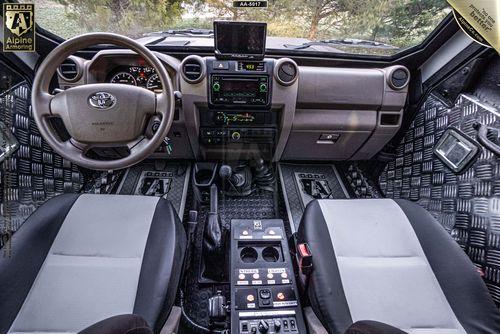 Interior view of a rugged SWAT APC CUDA featuring two seats, a steering wheel, dashboard controls, and various navigation and communication equipment. The floor is covered with diamond plate patterns.