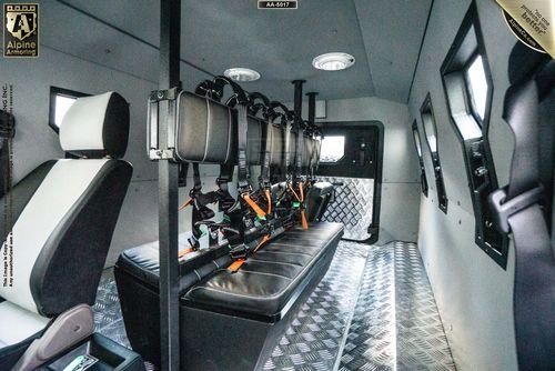 Interior of an armored SWAT CUDA APC featuring bench seating with harnesses, diamond plate flooring, and multiple windows.