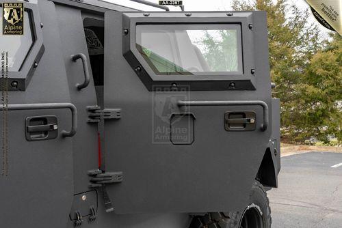 Close-up of the rear side of an armored bulletproof Pit-Bull VXT with logos and text from Alpine Armoring visible on the door and window, parked outdoors.