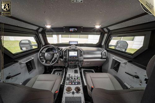 Interior view of an armored black Pit-Bull VXT featuring a steering wheel, dashboard with multiple control panels, two front seats, and side mirrors.