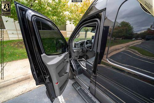 A black SWAT VAN - Pointer® Based on Ford Transit with the driver's door open, revealing the interior. The vehicle is parked on a driveway next to a grassy area and trees.