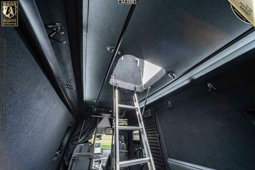 Interior of a Pointer Van Based on the Ford Transit with a retractable ladder leading through an open hatch in the roof, revealing an external environment. The setup includes dark upholstery and metallic fixtures.