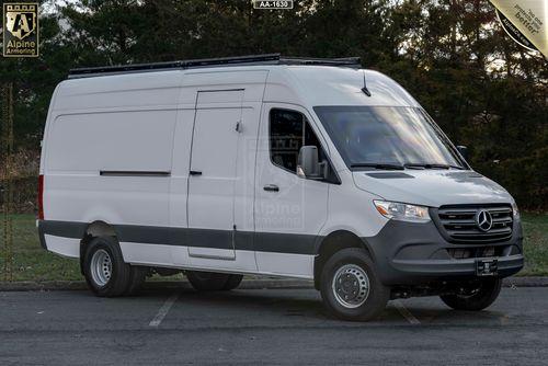 A white Mercedes-Benz Sprinter Pointer van is parked on a paved area with trees in the background. The van features a high roof and tinted windows.