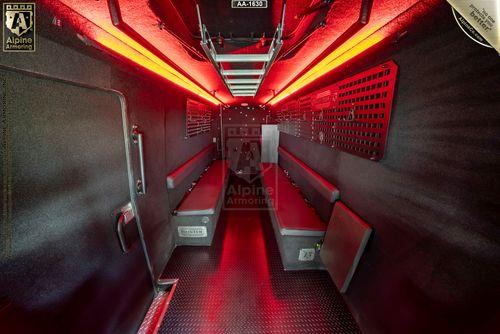 Interior of an armored SWAT Van - Pointer by Alpine Armoring, featuring red lighting, seating along the walls, and a metallic floor.