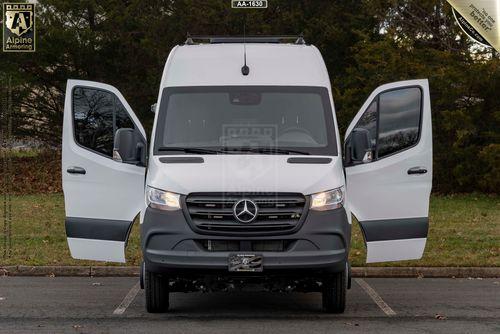 A white armored SWAT Van - Pointer® Based on Mercedes-Benz Sprinter with both front doors open, parked in an outdoor setting with trees in the background.