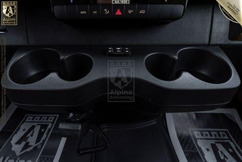 Close-up view of a Pointer van's center console featuring two cup holders and a small storage compartment between them, with "Alpine Armoring" branding visible on the floor mats.