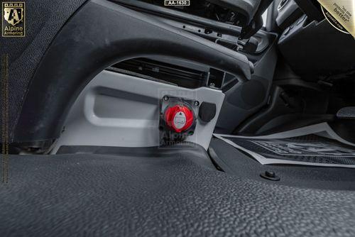 Close-up of a red safety latch located under the dashboard of an armored pointer based on Mercedes Sprinter 3500XD van. The interior is grey and black.