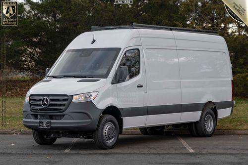 A white Mercedes-Benz Sprinter van is parked on a street with trees in the background.