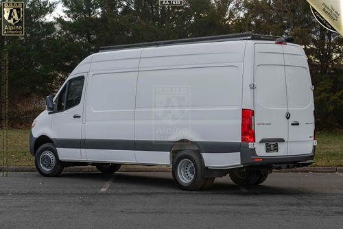 A white cargo SWAT Van - Pointer® Based on Mercedes-Benz Sprinter  is parked in a lot near trees. It has a high roof and no visible windows on the side, with branding for Alpine Armoring on the rear doors.