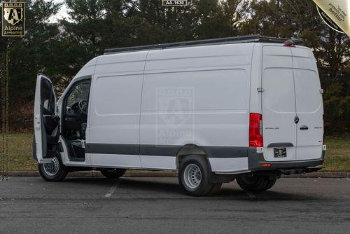 Side view of a white, high-roof armored Pointer van, with the driver door open, parked outside in a parking lot with trees in the background.