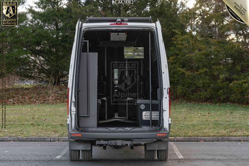 Back view of a parked white SWAT Van - Pointer® with its rear doors open, revealing a built-in cabinet and various equipment inside. Trees and grass are visible in the background.