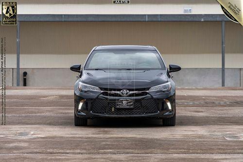 Front view of a black armored Toyota Camry XSE parked in an empty lot with a license plate holder.