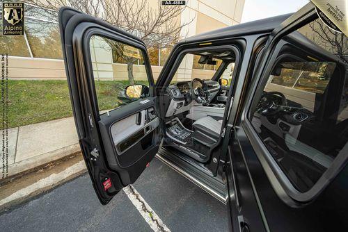 Open driver and passenger side doors revealing the black interior of a armored Mercedes-Benz G63 AMG SUV parked outside a commercial building.