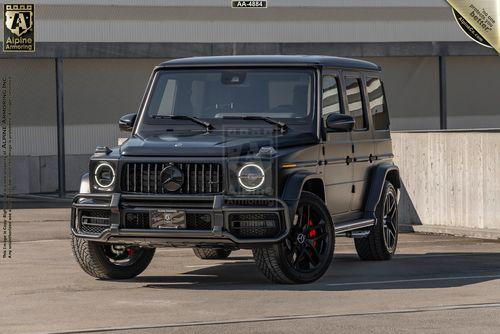 A black, armored Mercedes-Benz G63 AMG is parked outdoors on a concrete surface near a building. The SUV has dark tinted windows and alloy wheels.