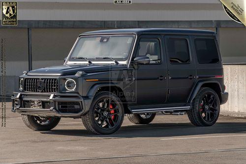 Matte black armored Mercedes-Benz G63 AMG SUV parked in an outdoor setting, featuring red brake calipers, dark tinted windows, and decorative badges.