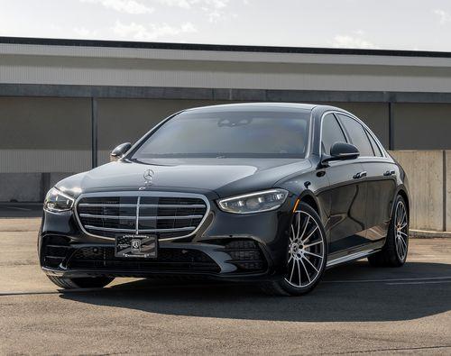 A sleek black, armored Mercedes-Benz S580 4MATIC from Alpine Armoring parked in an outdoor setting. The car features a modern design with a prominent front grille, stylish alloy wheels, and a polished exterior.