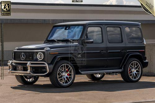 An armored black Mercedes G63 SUV with armoring by Alpine Armoring is parked in front of an industrial building, showcasing shiny rims and visible branding.