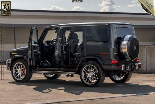 A black Mercedes G63 SUV with its doors open, parked in an outdoor setting. The vehicle has a spare tire mounted on the rear and a glossy finish.